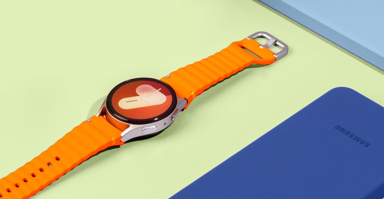 Photo of a Samsung Galaxy Watch with an orange strap on a yellow background. 